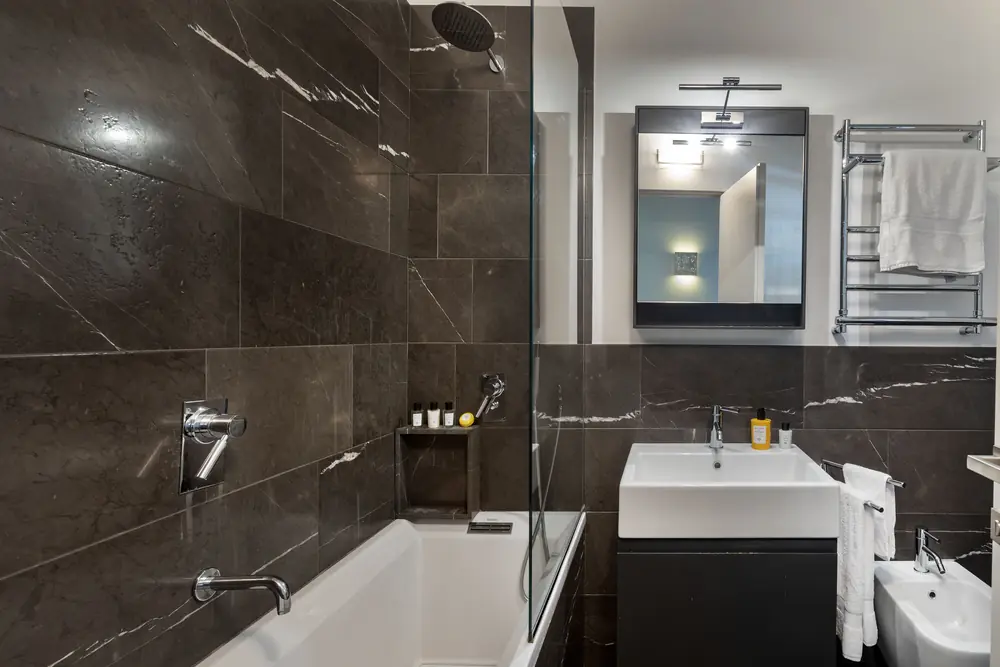 Bagno rivestito in marmo scuro con vasca e doccia